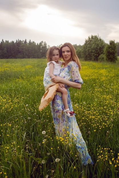 Madre e figlia in abiti e cappello stanno in un campo di fiori gialli nel giorno d'estate