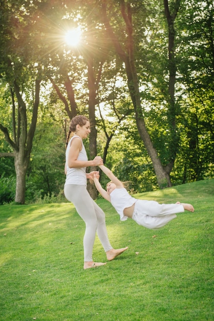 Madre e figlia in buona salute che giocano insieme nel parco. Movimento sopra la luce del sole sull'erba