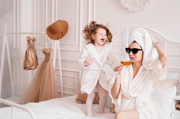 Madre e figlia in camera da letto in accappatoi figlia felice sta saltando