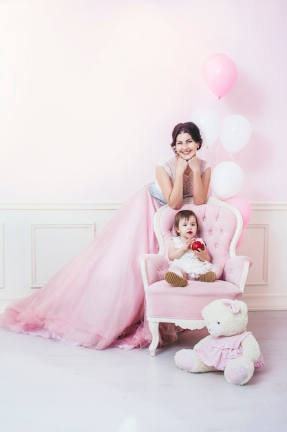 Madre e figlia in interni rosa con sedia vintage e palloncini in bei vestiti