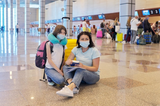Madre e figlia in maschere mediche protettive all'aeroporto con i bagagli