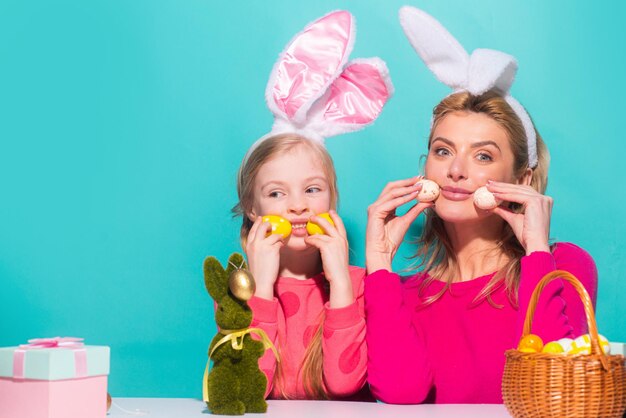 Madre e figlia in orecchie da coniglio a Pasqua che tengono le uova isolate su blue