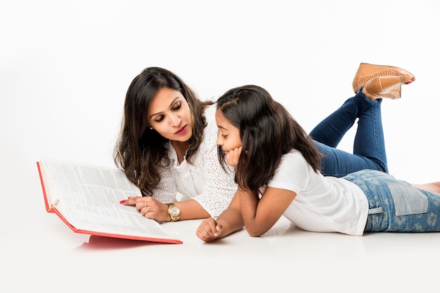 Madre e figlia indiane sdraiate sul pavimento con un libro, un laptop o un tablet che studiano o preparano una storia o giocano