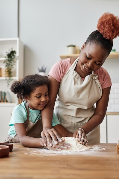 Madre e figlia nere felici che cuociono insieme nell'accogliente cucina domestica