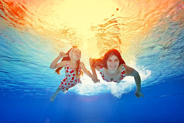Madre e figlia nuotano sott'acqua tenendosi per mano contro il tramonto arancione con gli stessi vestiti