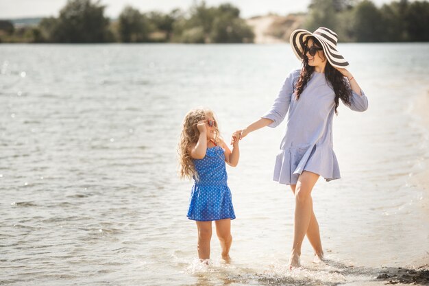 Madre e figlia piccola divertirsi sulla costa. Giovane bella mamma e suo figlio che giocano vicino all'acqua