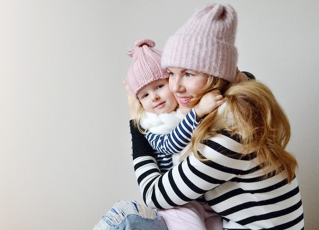 Madre e figlia piccola in cappelli e sciarpa su uno sfondo bianco, aspetto familiare