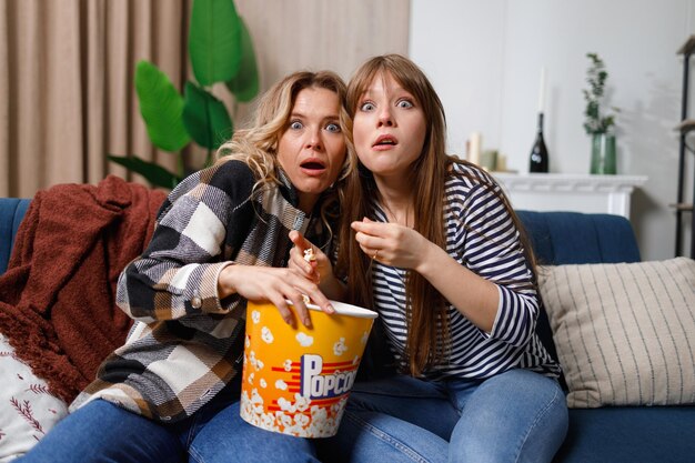 Madre e figlia si divertono a trascorrere il tempo libero insieme a casa guardando film spaventosi in TV e mangiando popcorn