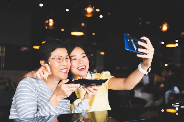 Madre e figlia sorridenti che si fanno un selfie con il cibo in un ristorante
