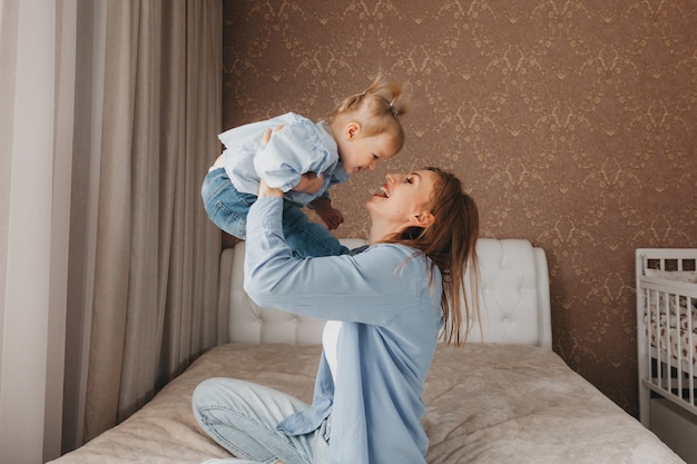 Madre e figlia stanno giocando e si divertono. Interno di casa, letto, una donna getta un bambino sul letto.