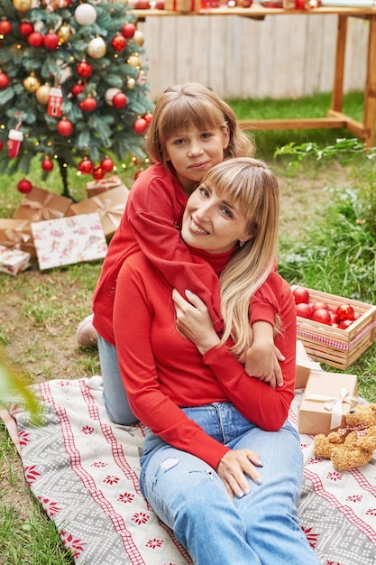 Madre e figlia vicino all'albero di Natale con regali, Natale in famiglia a luglio. Vacanze invernali e concetto di persone. Cartolina d'auguri di buon Natale e buone feste.