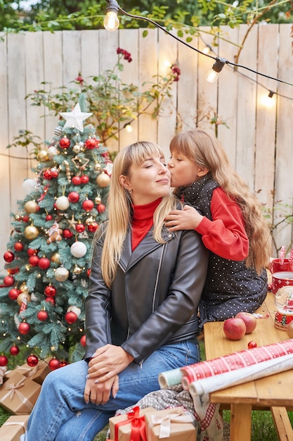 Madre e figlia vicino all'albero di Natale con regali, Natale in famiglia a luglio. Vacanze invernali e concetto di persone. Cartolina d'auguri di buon Natale e buone feste.