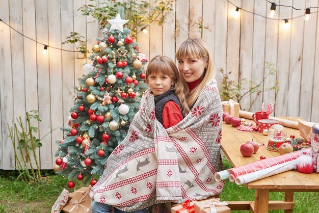 Madre e figlia vicino all'albero di Natale con regali, Natale in famiglia a luglio. Vacanze invernali e concetto di persone. Cartolina d'auguri di buon Natale e buone feste.