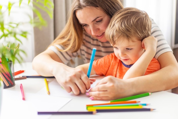 Madre e figlio che disegnano con le matite seduti alla scrivania a casa