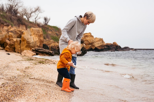 Madre e figlio piccolo trascorrono del tempo all'aperto in estate o in autunno insieme seduti sulla spiaggiaLa giovane madre gioca con il suo bambino sul lungomare Vacanze estive per due al mare