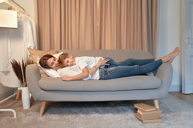Madre e figlio sdraiati sul divano mentre si abbracciano, giorno pigro, momenti di mamma e bambino