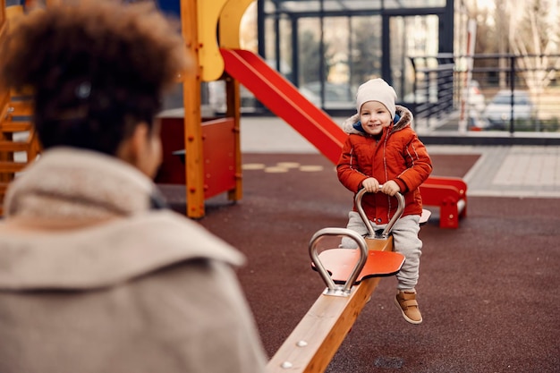 Madre e figlio si divertono su un'altalena nel parco giochi Felice ragazzino carino seduto su un'altalena con sua madre e si diverte