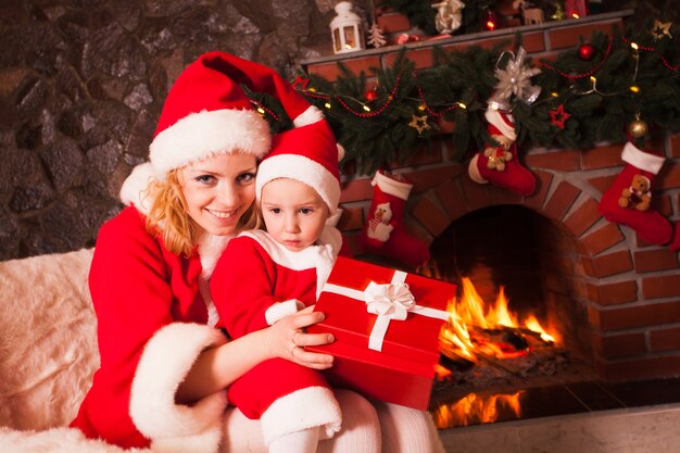 Madre e figlio sono seduti vicino al camino e all'albero di Natale. La famiglia guarda in una confezione regalo.