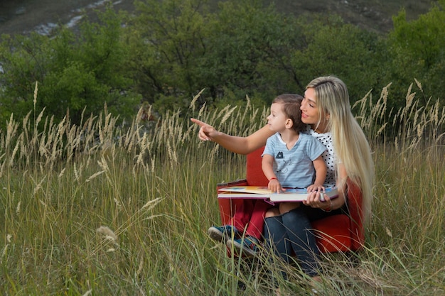 Madre e figlio sulla natura seduti sul divano a leggere un libro