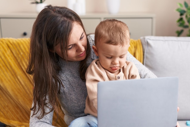 Madre e figlio utilizzando il computer portatile seduto sul divano di casa