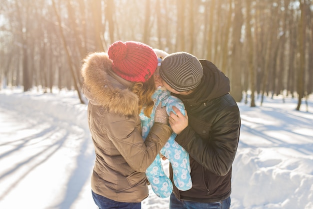 Madre e padre che tengono il loro bambino e lo baciano fuori in inverno.