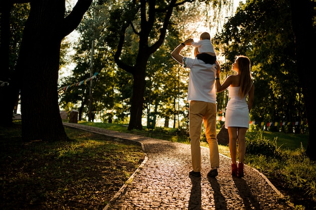 Madre e padre con un bambino sulle spalle che camminano nel parco verde