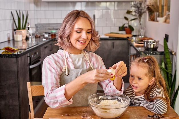 Madre e piccola figlia adorabile che cucinano insieme in cucina, bella mamma insegna ragazza carina del bambino che impasta la pasta per torta domestica preparando la sorpresa per la famiglia