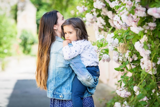 Madre e piccolo neonato bello che esaminano il cespuglio con le rose bianche