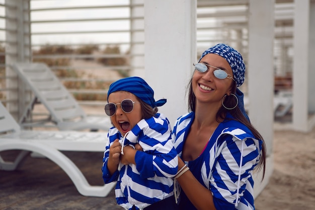 madre e suo figlio bambino in giacche blu a righe camminano lungo la spiaggia accanto a un gazebo in legno