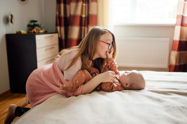 Madre felice che parla con il bambino sul letto Vista laterale della giovane donna con gli occhiali