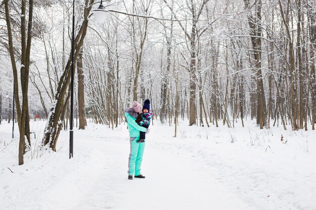 madre felice che tiene bambina sulla passeggiata nel bosco innevato di inverno