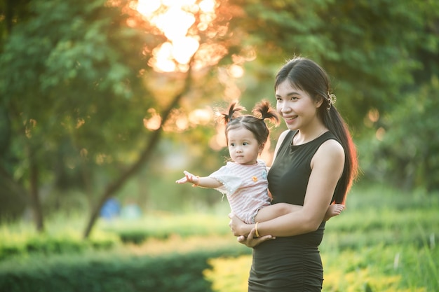 Madre felice che tiene il bambino sorridendo nel parco alla luce del sole fuori casa madre e figlia figlia in natura parco in estate sull'erba verde concetto bella madre e figlia copiare spazio per il testo