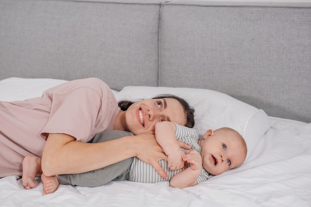 Madre felice con il bambino che si coccola a letto giocando a casa