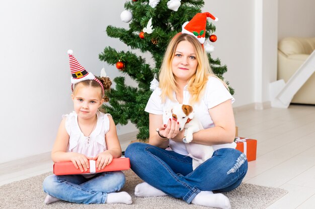 Madre felice con la figlia e il cane jack russell terrier seduto vicino all'albero di Natale