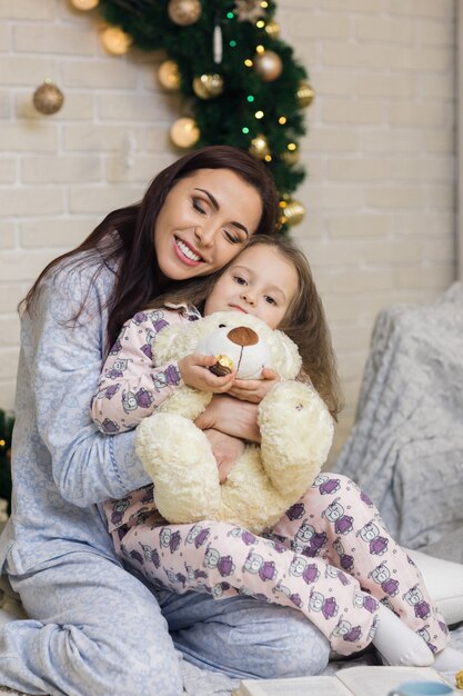 Madre felice con la figlia piccola che gioca vicino all'albero di Natale