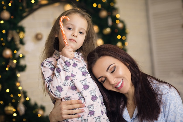 Madre felice con la figlia piccola che gioca vicino all'albero di Natale