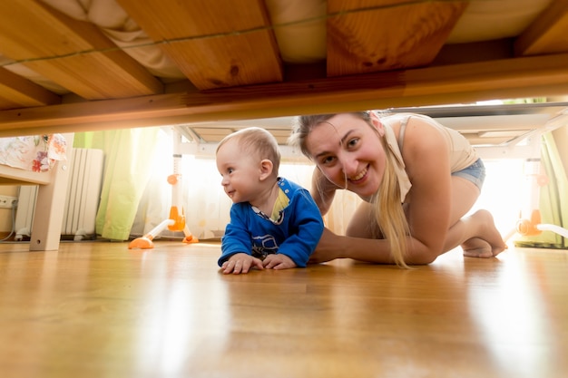 Madre felice e bambino che guardano sotto il letto