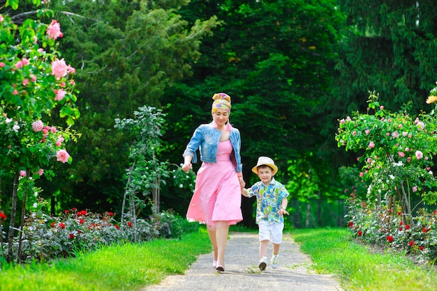 Madre felice e figlio che camminano nel parco estivo con fiori.