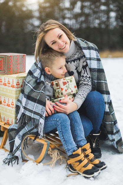 Madre felice e figlio che hanno divertimento con la slitta in una foresta di inverno