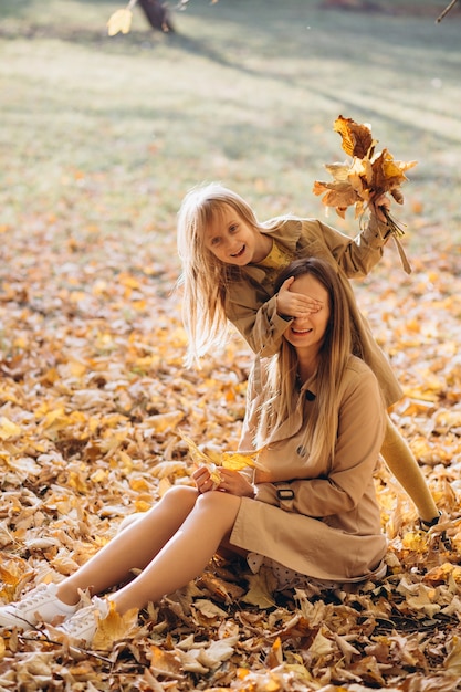 Madre felice e la sua bellissima figlia seduti e divertirsi tra le foglie gialle nel parco d'autunno.