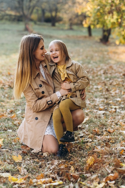 Madre felice e la sua bellissima figlia seduti e divertirsi tra le foglie gialle nel parco d'autunno.