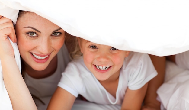 Madre felice e la sua ragazza bionda che giocano insieme su un letto