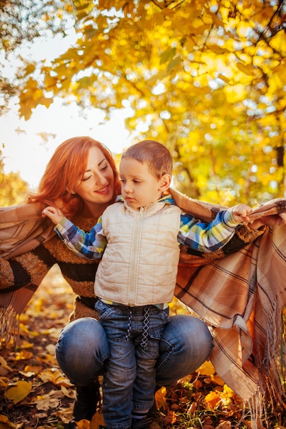 Madre felice e suo figlio piccolo che abbraccia e si diverte nella foresta di autunno