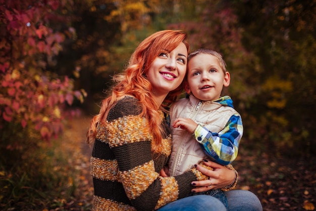 Madre felice e suo figlio piccolo divertirsi nella foresta d&#39;autunno Abbracciare mamma e bambino