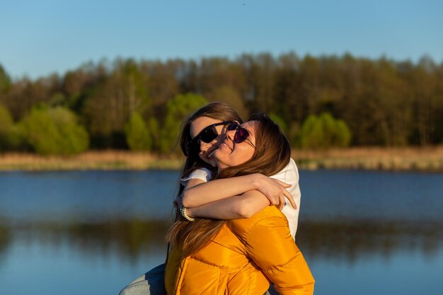 Madre giocosa che dà alla figlia sulle spalle un giro in riva al lago di primavera