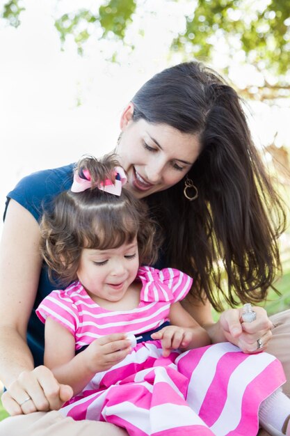 Madre giovane di razza mista e bambina carina che si applicano la lucidatura per le unghie nel parco