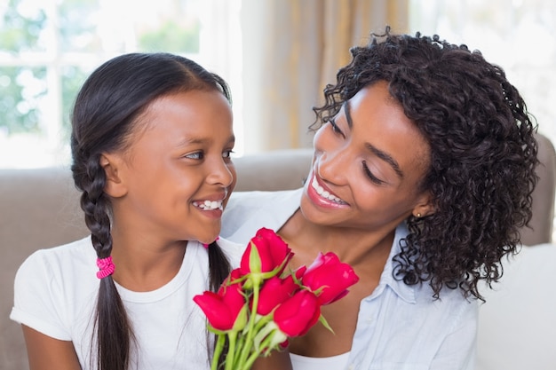 Madre graziosa che si siede sullo strato con sua figlia che tiene le rose