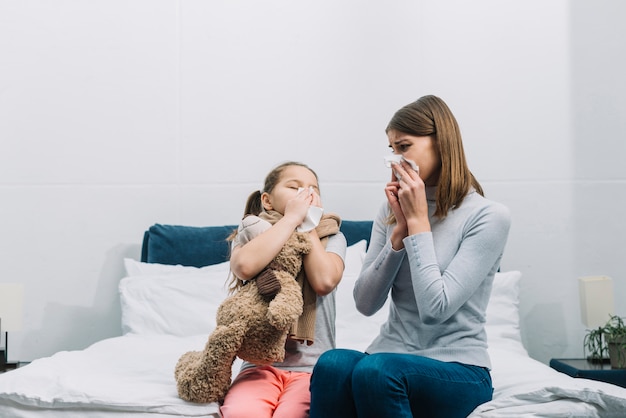 Madre guardando sua figlia che soffia il naso con la carta velina