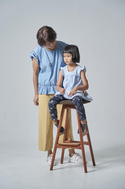 Madre in piedi dalla figlia seduta su uno sgabello sullo sfondo grigio