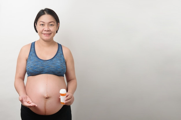 Madre incinta asiatica felice nella faccina sorridente che tiene e mostra che tiene un sacco di pillole, vitamina, isolato su sfondo bianco, concetto di gravidanza